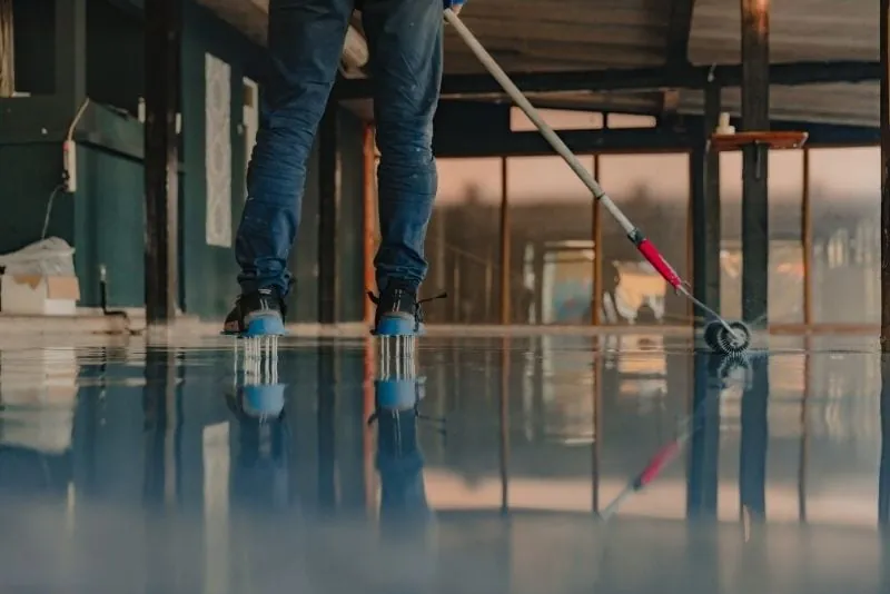 Installer smoothing a freshly poured blue-grey epoxy floor with a spiked roller