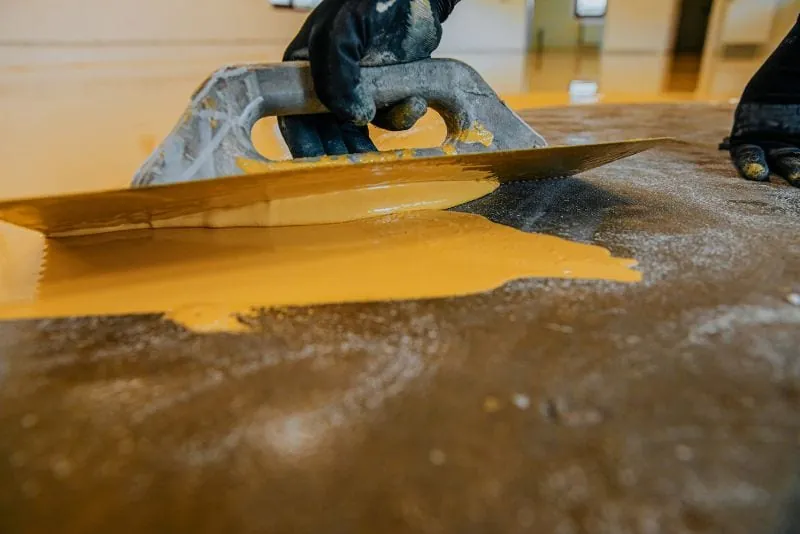 Concrete floor being coated with a yellow epoxy overlay in Wollongong