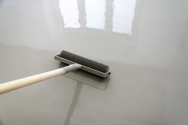 Notched trowel tool spreading a grey epoxy floor coating