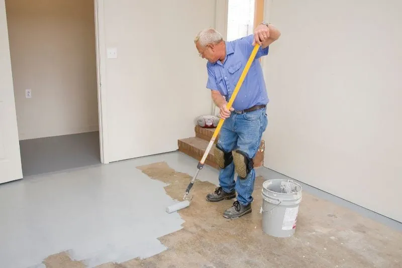 Painter rolling grey floor coating across a bare interior floor