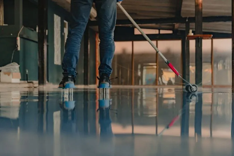 Installer smoothing a freshly poured blue-grey epoxy floor with a spiked roller