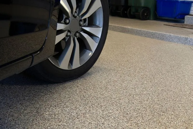 Car wheel resting on a speckled beige flake epoxy garage floor